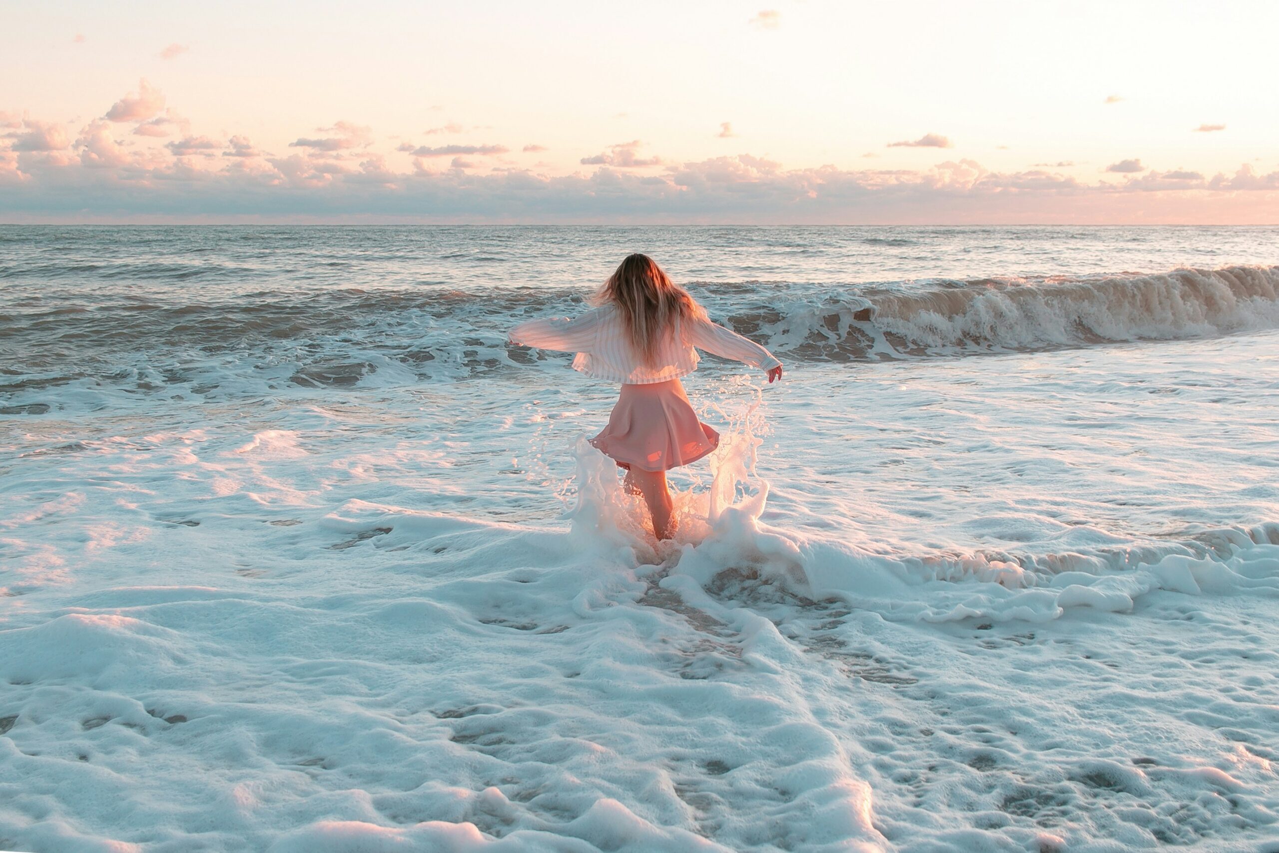 Woman runs into ocean n a flowing skirt and cardigan demonstrating the release of the emotional pain body